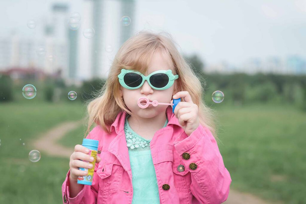 Portrait of a cheerful girl blowing soap bubbles outdoors - Fotoğraf, Görsel
