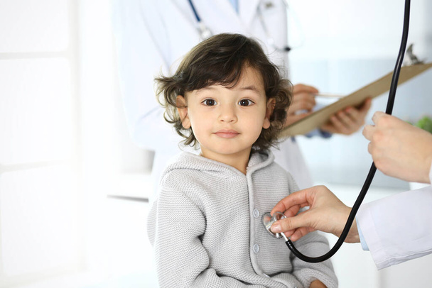 Doctor examining a child patient by stethoscope. Cute arab boy at physician appointment. Medicine and healthcare concept - Foto, Imagen