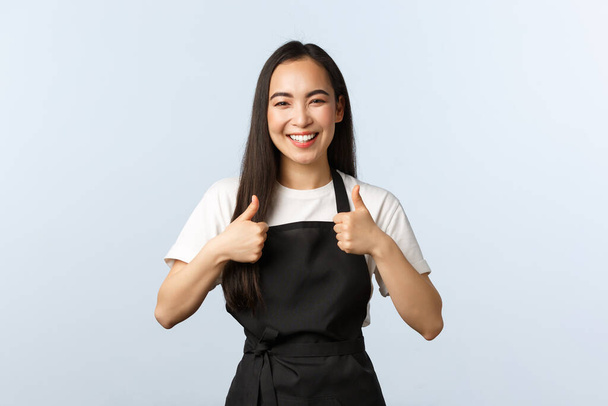 Koffieshop, kleine bedrijven en startup concept. Vrolijk glimlachend Aziatisch vrouwelijk café personeel, barista aan het werk met duim omhoog, met schort aan. Schattig meisje werknemer aanbevelen bezoek mooie plek, goed eten - Foto, afbeelding