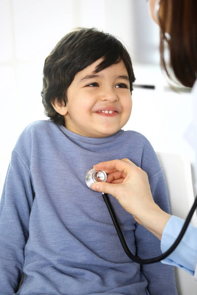 Doctor examining a child patient by stethoscope. Cute arab boy at physician appointment. Medicine and healthcare concept - Photo, Image