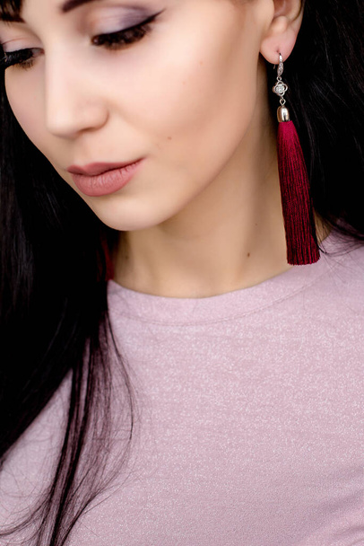 Close-up view of the elegant face of a young woman with neat makeup ,black hair and long maroon earrings - Фото, изображение