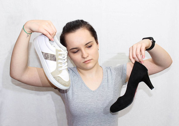 Kızın elinde bir spor ayakkabı ve yüksek topuklu bir ayakkabı var. Ayaklarına ne giyeceğini seçiyorsun.. - Fotoğraf, Görsel
