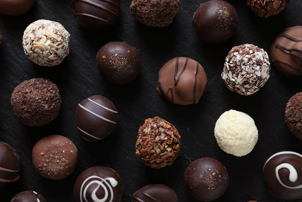 Verschillende smakelijke chocolade snoepjes op zwarte tafel, plat gelegd - Foto, afbeelding