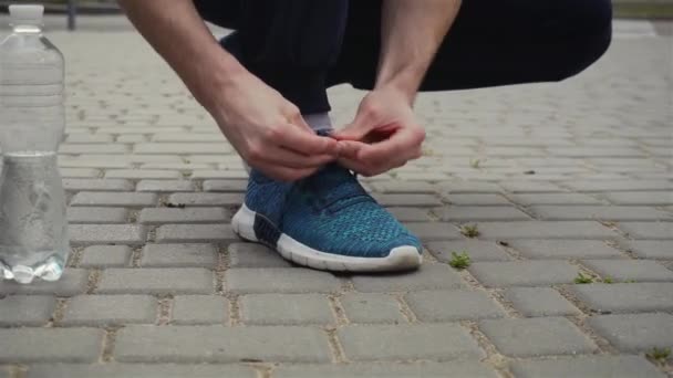 Чоловік зв'язує шнурки на спортивне взуття під час кардіо-тренувань і пляшка води поруч
 - Кадри, відео