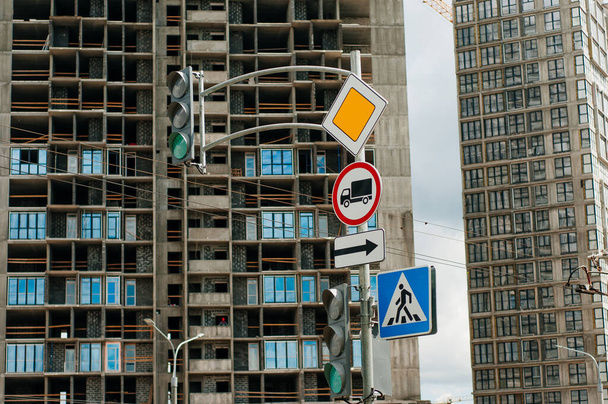 Útjelző táblák: főút, gyalogos átkelőhely, megállás tilos. A háttérben az építés alatt álló város. - Fotó, kép