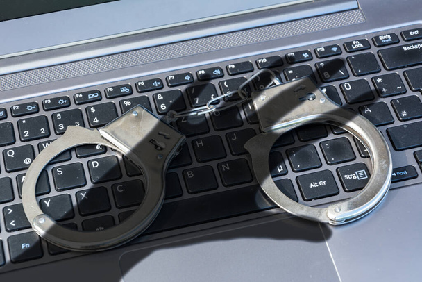 Handboeien op een toetsenbord plus donkere schaduw van een hand die cybercriminaliteit symboliseert - Foto, afbeelding