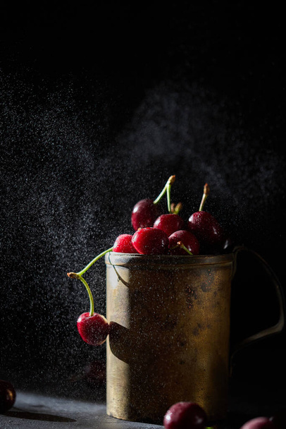 Cherry berries in a copper mug, spray on the background. - Фото, зображення