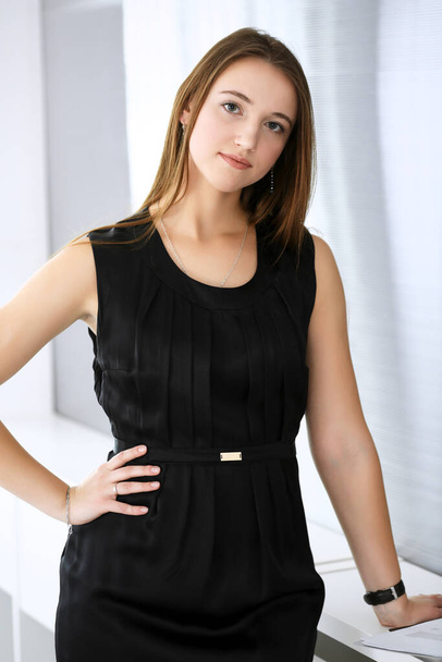 Business woman standing and looking at camera in office of highlight background. Headshot of beautiful girl in black dress - Zdjęcie, obraz