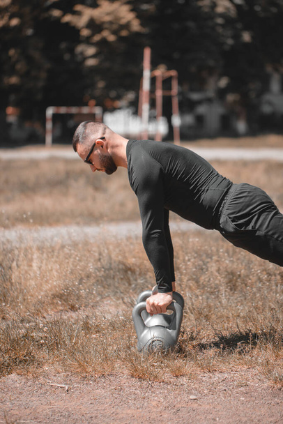 Exercice extérieur. Athlète masculin faisant de l'exercice avec kettlebell dans le parc. - Photo, image