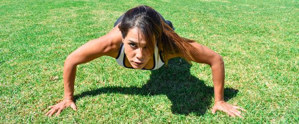Молодая спортсменка, тренируется на открытом воздухе, делает отжимания в парке
 - Фото, изображение