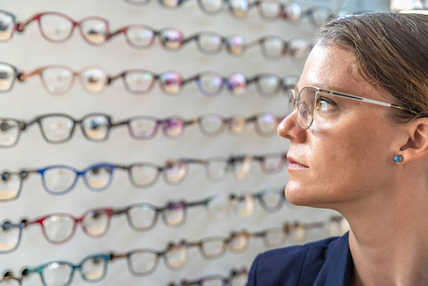 τα γυαλιά επιλέγονται και ελέγχονται από μια γυναίκα σε ένα κατάστημα οπτικών. αντίγραφο χώρου - Φωτογραφία, εικόνα