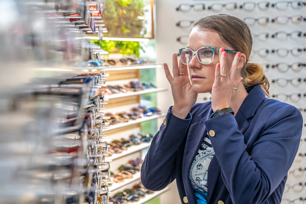 Mladá atraktivní žena v obchodě s optikou si zkouší nové brýle. kopírovat prostor - Fotografie, Obrázek