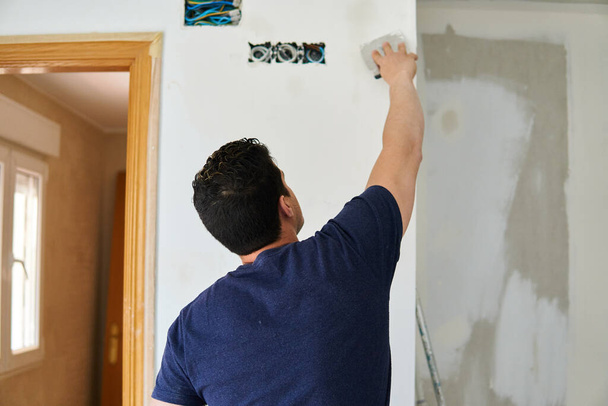 Pintor trabajando con espátulas en una habitación blanca
 - Foto, Imagen