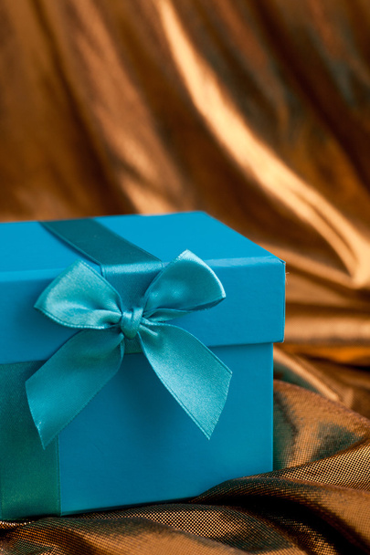 Blue gift box with a bow on gold fabric - Fotoğraf, Görsel