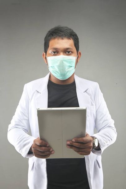 novo homem malaysian normal médico covid-19 usando máscara facial segurando comprimidos computador isolado em fundo cinza. Yogyakarta indonesia. 29 de setembro de 2020 - Foto, Imagem