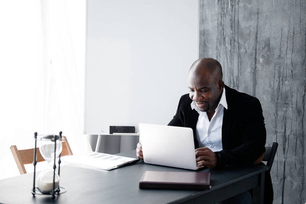 Dark-skinned fellow in a business suit working at a laptop in the office. The employee is African American in a major law firm. - Foto, Bild