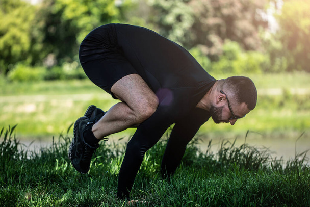 Homem esticando as mãos e pernas na grama verde no parque. O atleta faz exercícios ao ar livre. Esporte, ioga, pilates, fitness, conceito de estilo de vida saudável
. - Foto, Imagem
