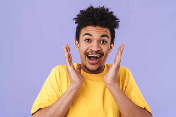 Фотографія збудженого афроамериканського чоловіка, який висловлює здивування на фотоапараті, відокремленому над пурпуровим фоном. - Фото, зображення