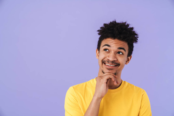 Photo of joyful african american man smiling and looking upward isolated over purple background - Foto, Imagem