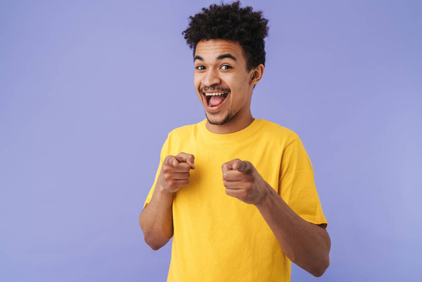 Photo of excited african american man smiling and pointing fingers at camera isolated over purple background - Photo, Image