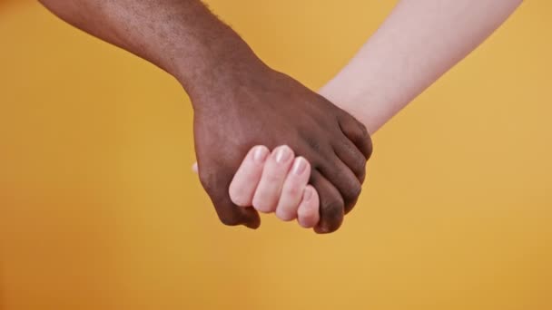 mani bianche e nere che tengono insieme isolate sullo sfondo arancione. Da vicino. - Filmati, video