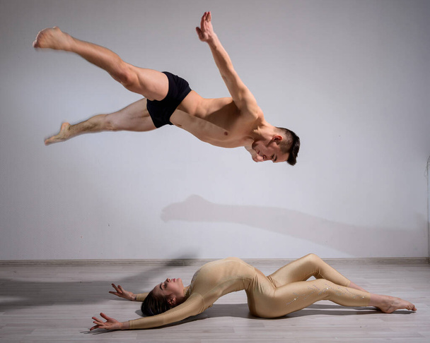 Acrobatic couple perform number on a white background. A duet of gymnasts rehearsing a performance with support. A man and a very flexible woman are dancing. - Fotó, kép