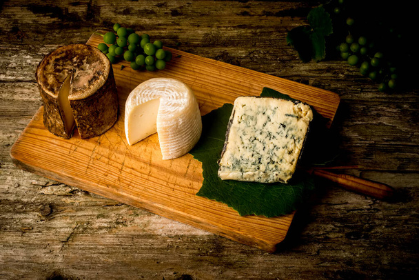 Három fajta kézműves sajt Észak-Spanyolországból egy fa asztalon, csendélet. - Fotó, kép