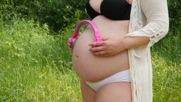 Mulher colocando fones de ouvido em sua barriga grávida, desfrutando de música favorita com bebê
 - Filmagem, Vídeo