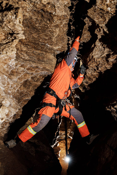Спелеолог спускается по веревке в глубоком вертикальном туннеле пещеры. Пещерный человек висит над пропастью. Вид сверху на туннель
. - Фото, изображение