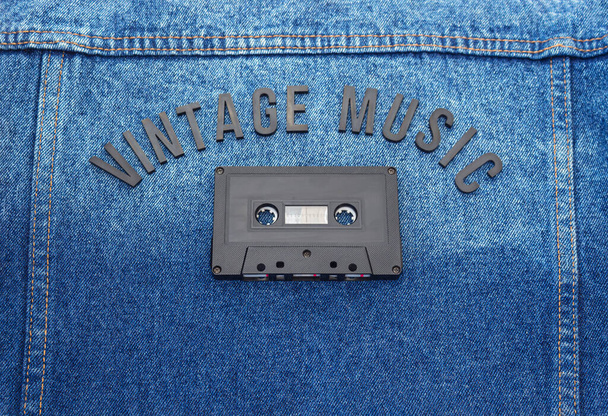 ジーンジャケットの上に古いブラックカセットが付いたVINTAGE MUSICのブラックレタリングワードのトップビュー。ファッションと音楽のコンセプト - 写真・画像