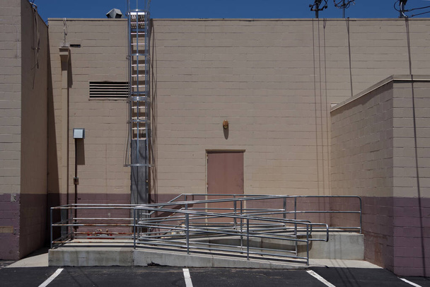 O lado traseiro de um edifício de armazenamento comum com uma porta traseira, uma rampa e uma escada para o telhado
 - Foto, Imagem
