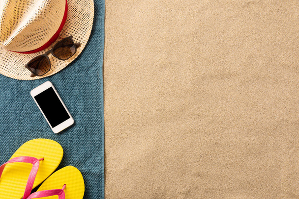 Summer vacation composition. Flip flops, and smartphone on sand background. Travel vacation concept. Summer background. Border composition made of towel - Foto, Bild