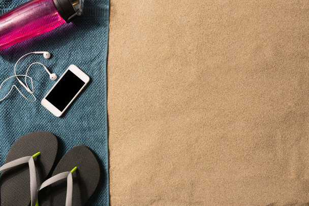 Sommermode, Sommeroutfit auf Sandgrund. Schwarze Flip-Flops und Smartphone. Flache Lage, Draufsicht - Foto, Bild