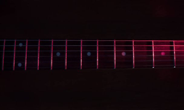 close-up para um seis cordas de guitarra elétrica preta e painéis de madeira iluminados com luzes vermelhas Instrumentos e conceito de música
 - Foto, Imagem