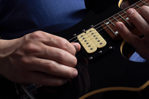 Primo piano di un uomo che indossa una t-shirt blu navy suonando una chitarra elettrica nera e gialla con sfondo in legno. Concetto rock & roll e musica
 - Foto, immagini