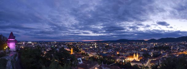 City lights of Graz and the famous clock tower (Grazer Uhrturm) on Shlossberg hill, Graz, Styria region, Austria, after sunset. Panoramic view. - Photo, Image