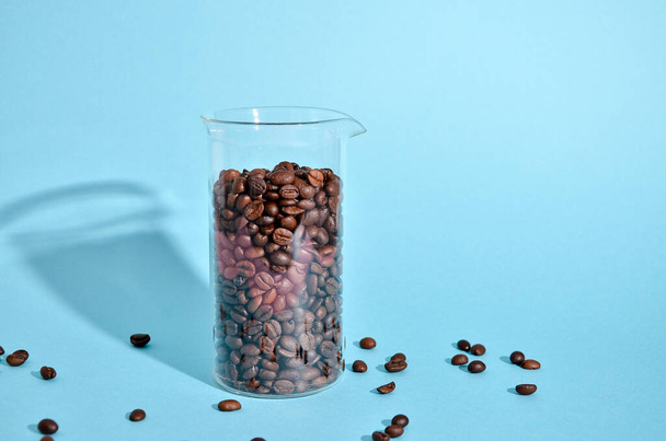 Coffee beans spilling out of a cristal jar on mint blue color background. Pastel colored wallpaper, trendy fashion photography - 写真・画像