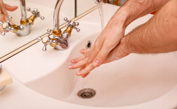 Junger Mann wäscht sich im modernen Waschbecken die Hände mit Seife und Schaumstoff, um sich vor dem Coronavirus oder Covid 19 zu schützen. Hygienekonzept für Badezimmer. - Foto, Bild