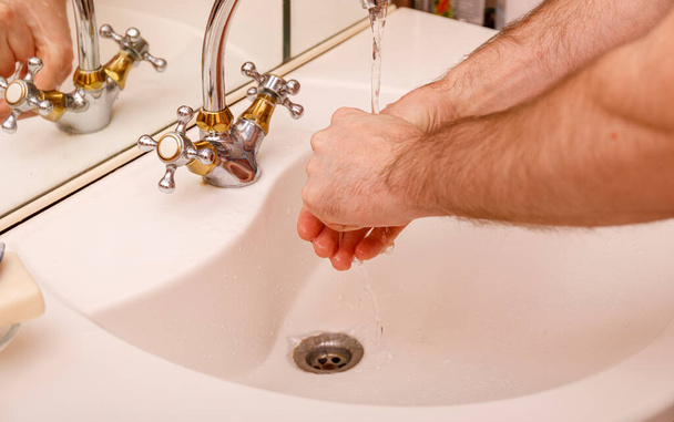 Młody człowiek myje ręce w nowoczesnym zlewie mydłem i piankami do prania w celu ochrony przed koronawirusem lub covid 19. Koncepcja higieny łazienki. - Zdjęcie, obraz
