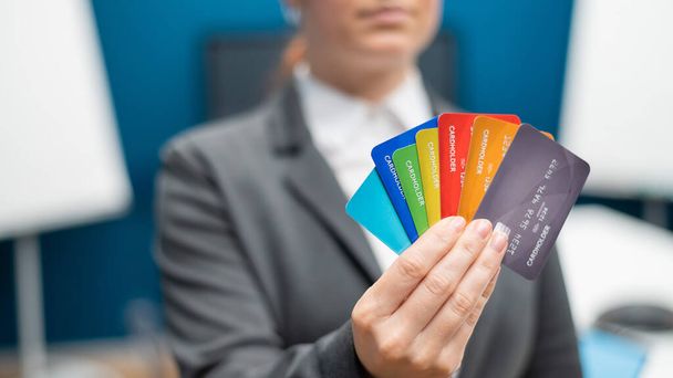 Unrecognizable woman dressed in a suit holds multi-colored plastic credit cards. A faceless bank employee offers a loan. Shopping concept. Close-up of female hands with debit cards. - Photo, image