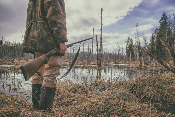 Avcı ormandaki bataklıkta duruyor ve elinde eski bir av tüfeği tutuyor. - Fotoğraf, Görsel