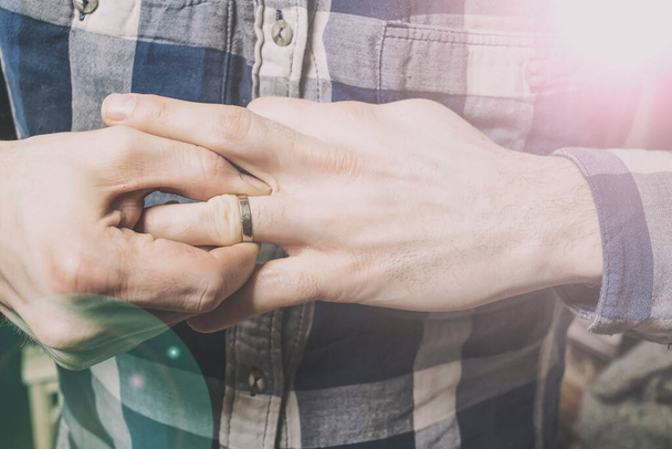 un hombre que lucha por quitarse el anillo de bodas de su dedo. Mano izquierda Versión católica
  - Foto, Imagen