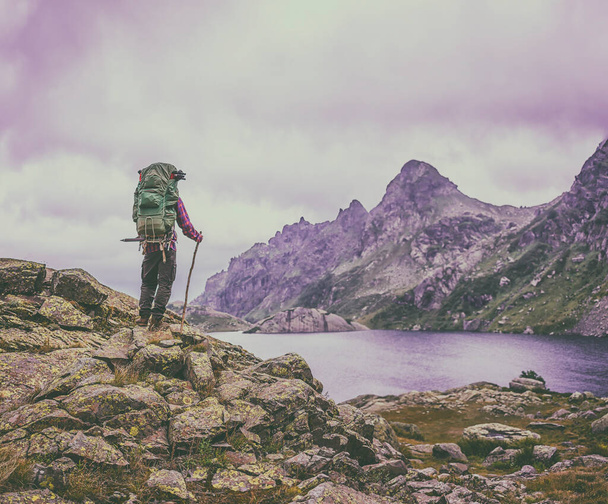 homem com uma mochila em pé no fundo vintage de altas montanhas afogando-se em nuvens e lago claro
 - Foto, Imagem