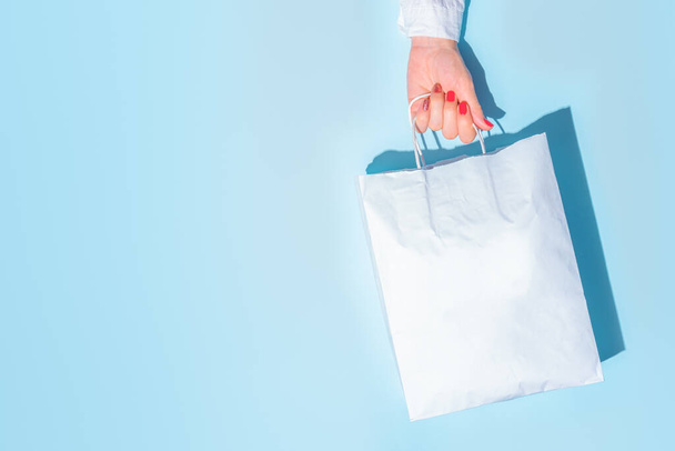 hand holding shopping paper bag. Concept of consumerism, shopping symbol. Copy space trend pastel color. Hard shadows, morning light. - Photo, image