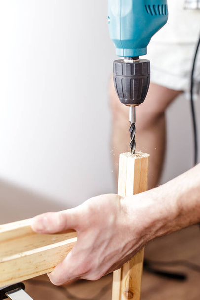 Чоловік свердлить отвір електричний дриль в дерев'яній дошці вдома у вітальні
 - Фото, зображення