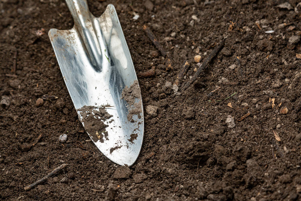 A metal shiny small garden shovel is on freshly plowed ground. Horizontal orientation. Space for text. - Photo, Image
