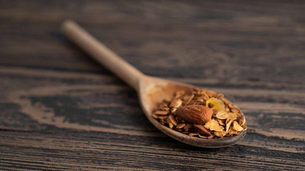 one standalone wooden spoon serving of granola with nuts. blurred wooden background. place for text. small portion - Fotoğraf, Görsel