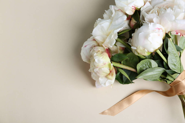 Bouquet of beautiful peonies with ribbon on beige background, flat lay. Space for text - Foto, Bild