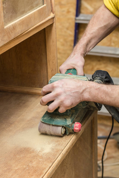 Ξυλουργός αποκαθιστά vintage το ξύλινο ένα μπουφέ από ένα ηλεκτρικό της μηχανής λείανσης. - Φωτογραφία, εικόνα