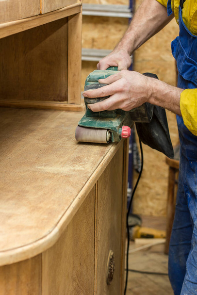 Ξυλουργός αποκαθιστά vintage το ξύλινο ένα μπουφέ από ένα ηλεκτρικό της μηχανής λείανσης. - Φωτογραφία, εικόνα
